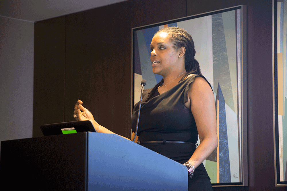 person stands at podium and speaks while gesturing with hand