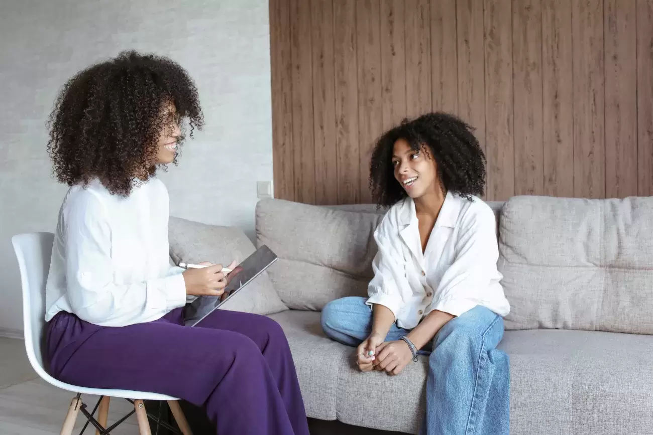 one person sits on a couch and talks to a therapist holding a clipboard who is taking notes