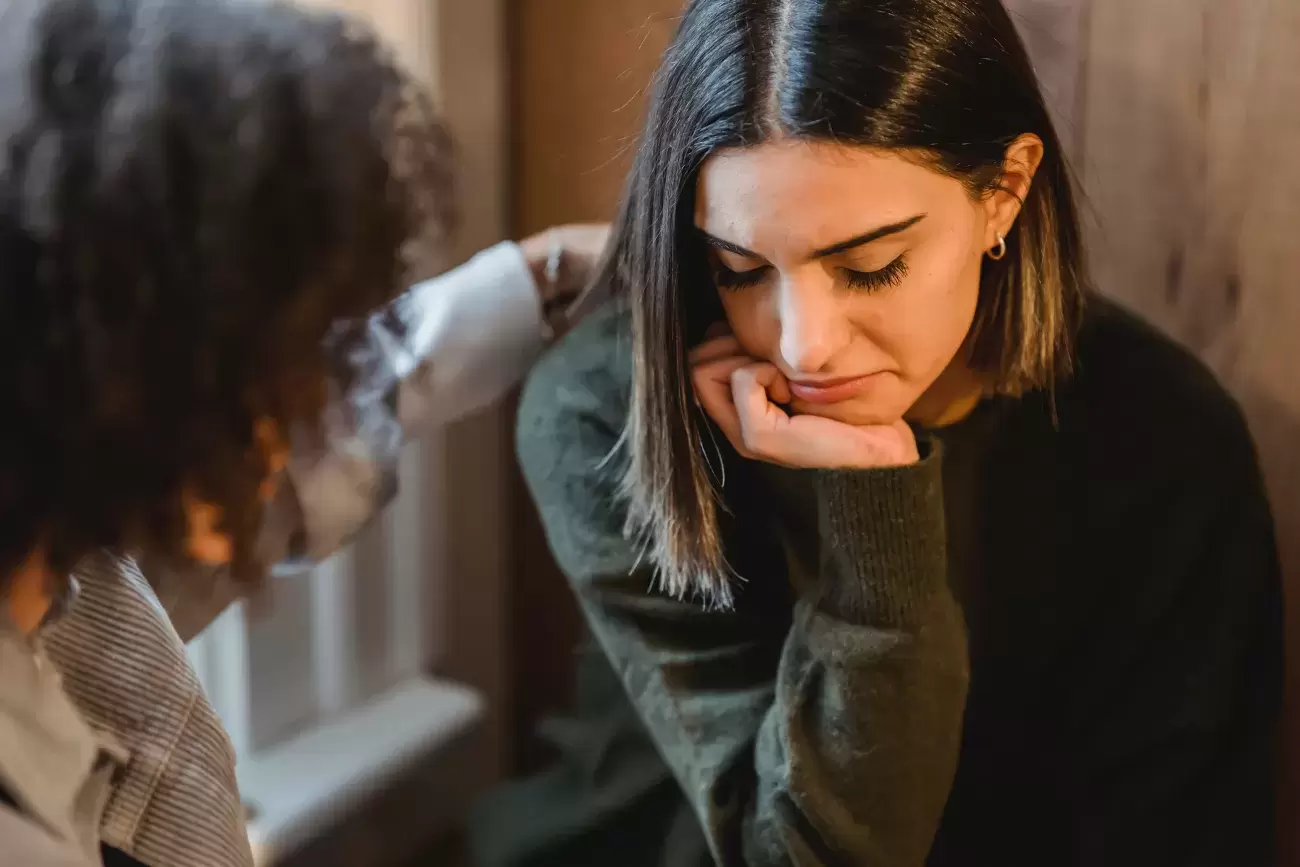 one person consoles another who is looking down, clearly upset