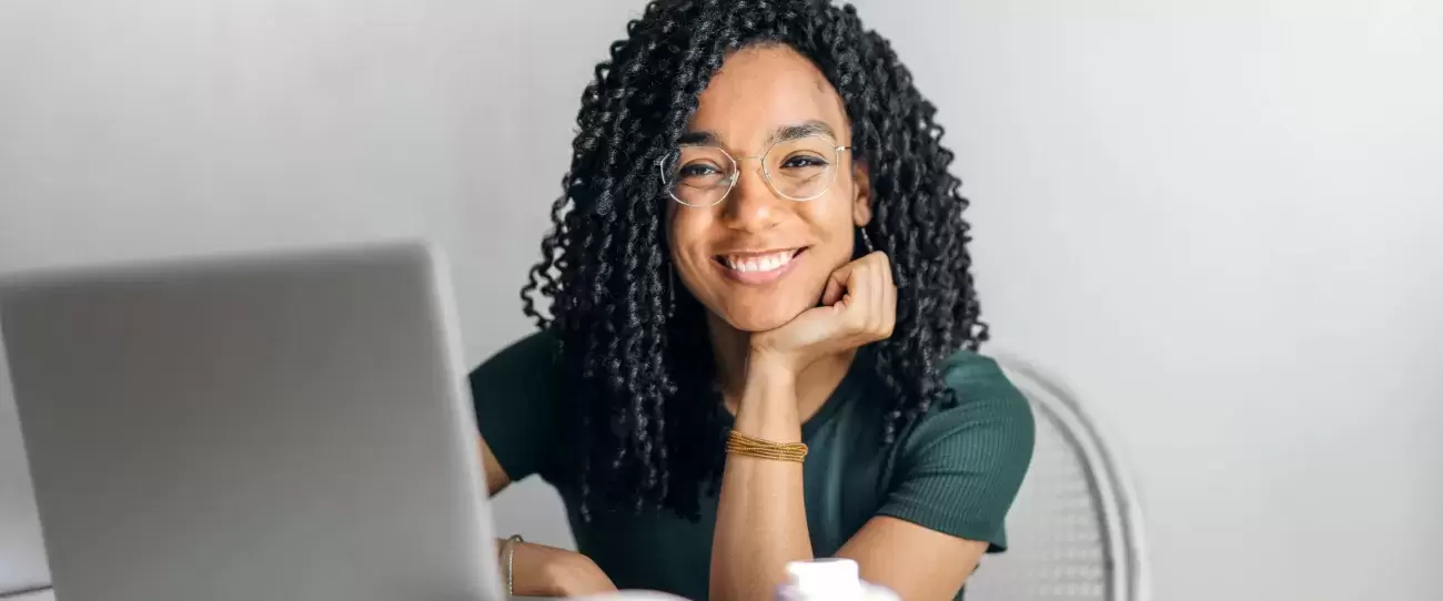 person smiles from behind laptop