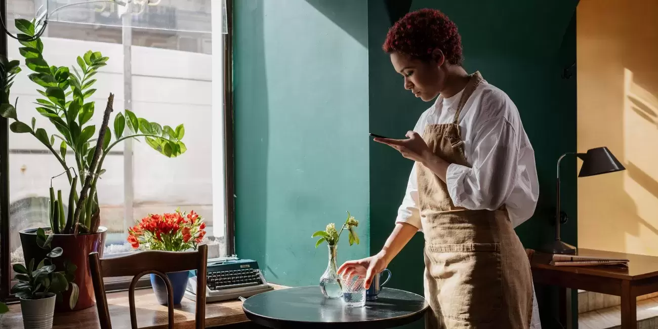 restaurant server in apron sets down glass of water while looking worriedly at phone