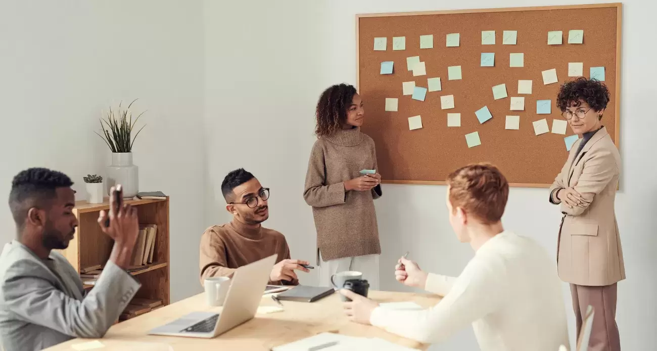 group of people works together at a table and at a bulletin board with post-it notes on it