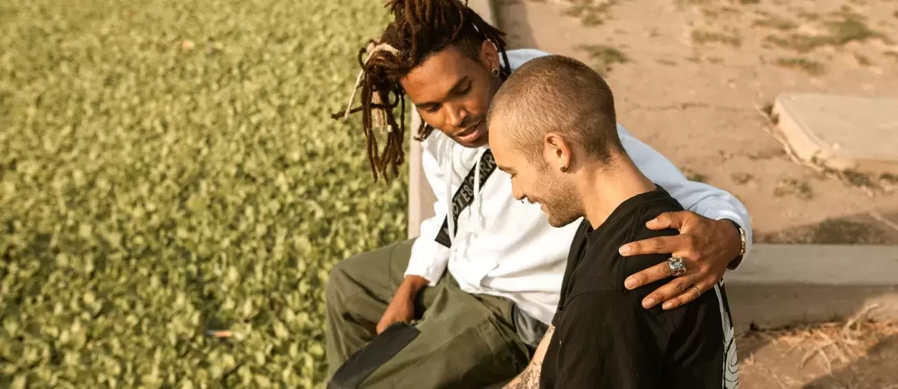 two people sit and talk while one puts their arm around the other in concern