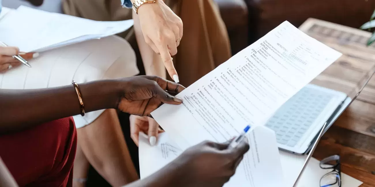 two hands hold a piece of paper with text on it, other hands point at it