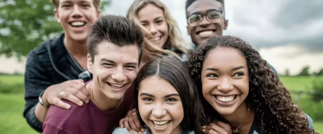 kids, teens, and young adults stand in huddle smiling