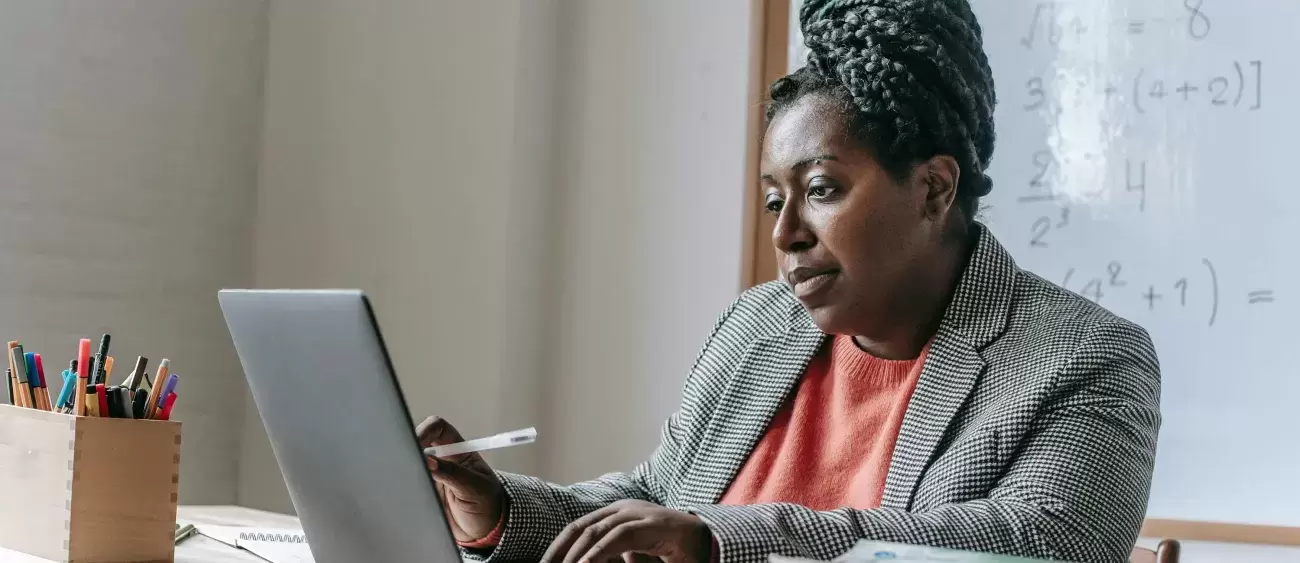 teacher sits at classroom desk watching laptop