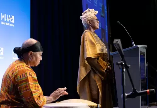 One person plays drum while another stands at podium