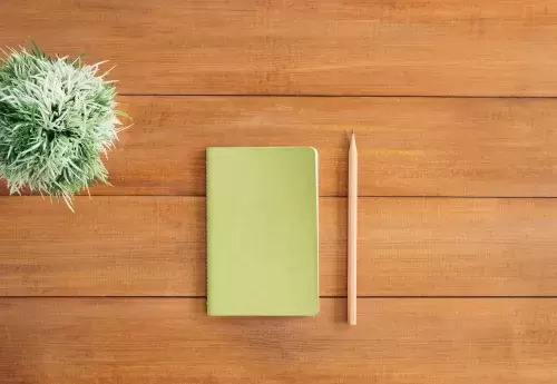 notebook and pencil on wood table next to green plant