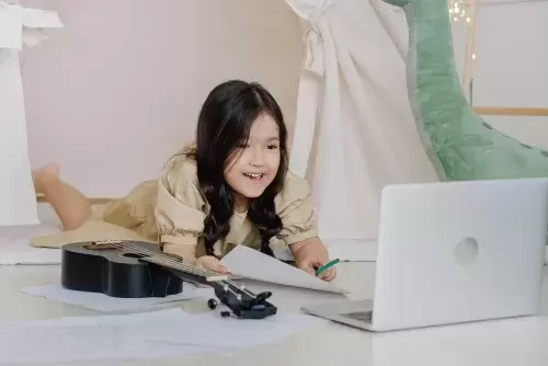 young child looks at laptop with ukelele next to them