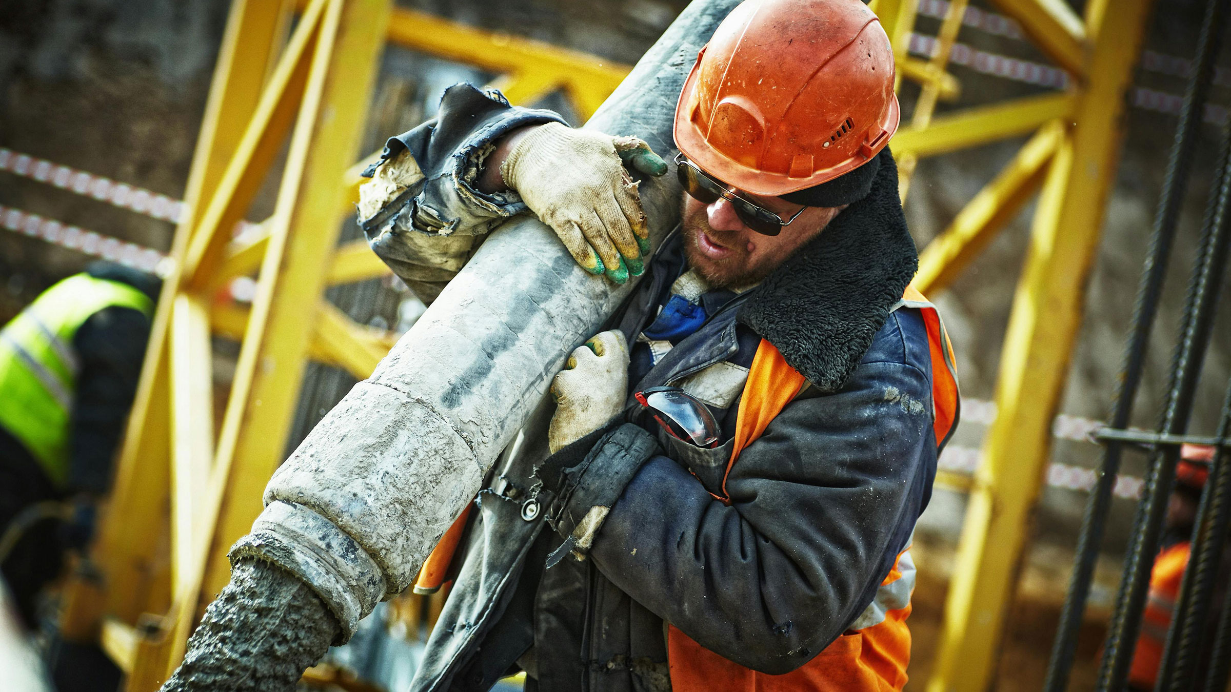 construction worker wearing orange helmet holds large pipe